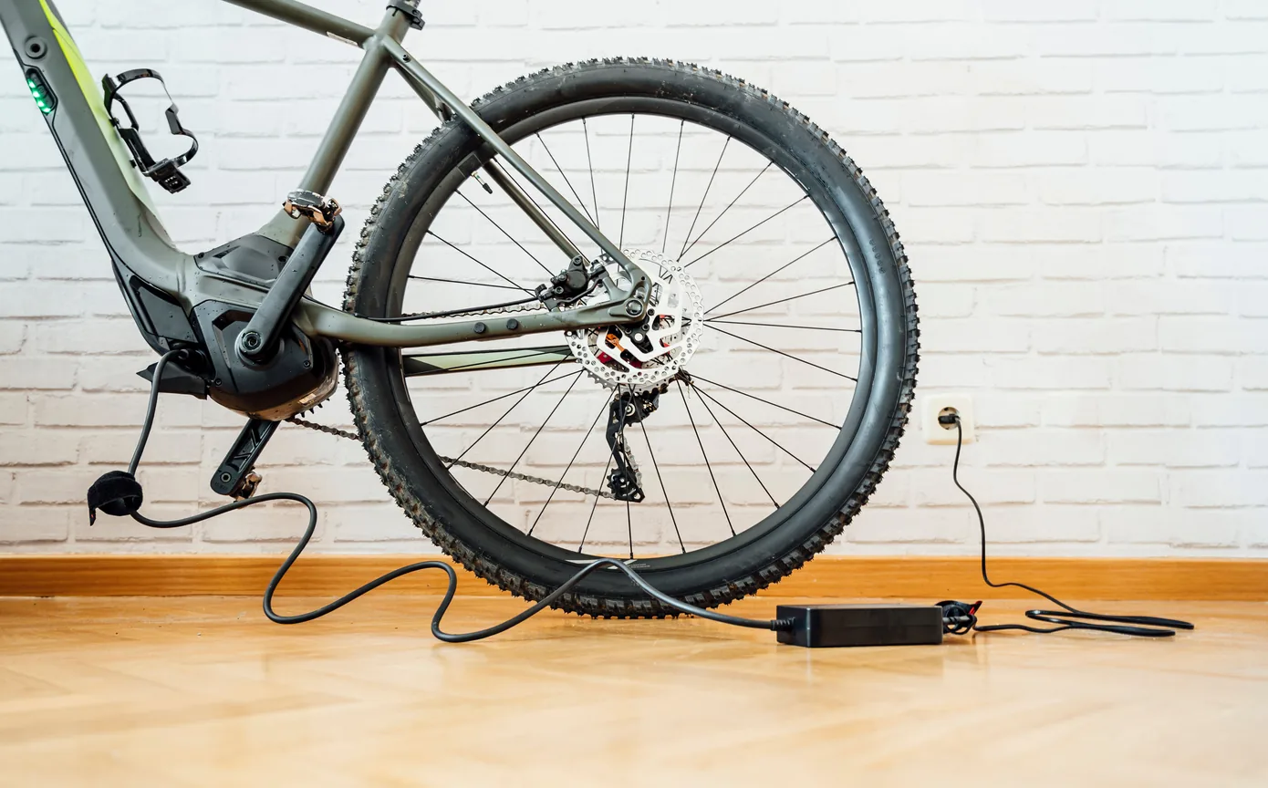 E-bike plugged into a wall outlet to charge beside a white brick wall E-bike plugged into a wall outlet to charge beside a white brick wall