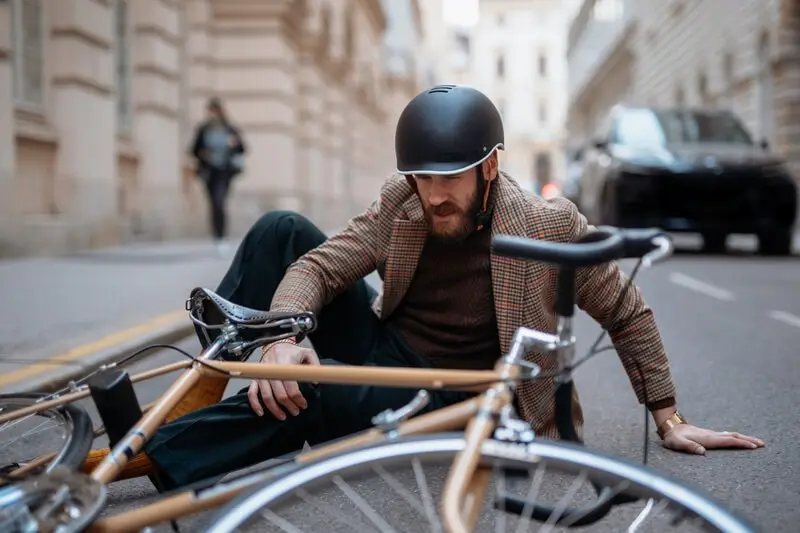 Commuter in a helmet on the pavement after crashing a bike on a city street Commuter in a helmet on the pavement after crashing a bike on a city street